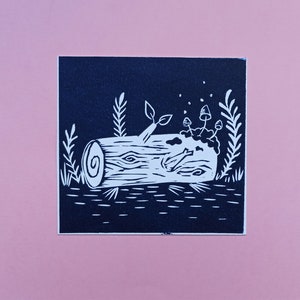 Peut inclure: Une linogravure en noir et blanc représentant un tronc d'arbre avec des champignons et du feuillage. Le bout du tronc montre un motif de grain en spirale. L'impression est sur fond rose.