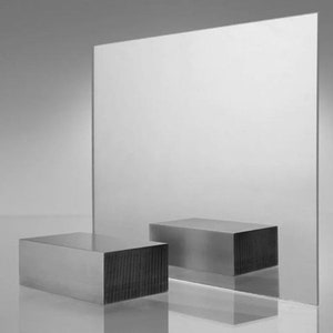 Peut inclure: Deux blocs rectangulaires argentés, l'un devant l'autre, sur une surface blanche devant un grand miroir argenté.