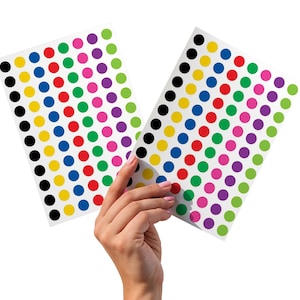 以下が含まれることがあります： カラフルなドットステッカーのシートが2枚。各シートには、黒、黄、青、赤、緑、ピンク、紫のドットが並んでいます。