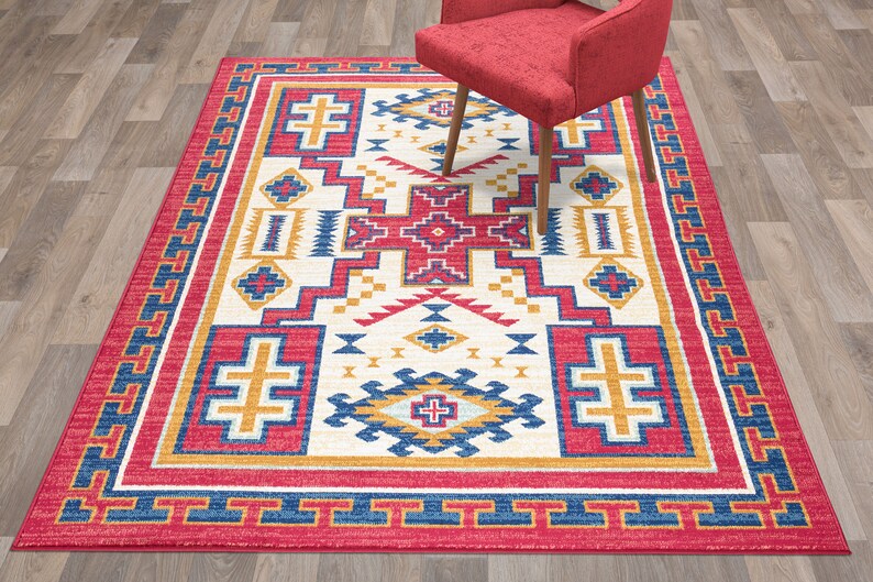 May include: A Southwestern-style area rug with a white background and a geometric pattern in shades of red, blue, and yellow. The rug has a red border with a blue and yellow geometric pattern.