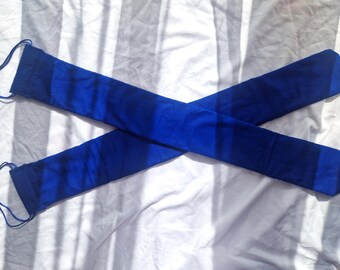 Puede incluir: Dos bolsas largas de tela azul real con cierres de cordón, dispuestas en forma de X sobre un fondo blanco texturizado. Las bolsas parecen estar hechas de un material suave, y los cordones son de un azul a juego.
