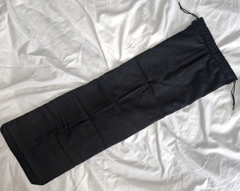 Puede incluir: Una bolsa negra de cordón hecha de tela. La bolsa está tendida sobre una superficie blanca.