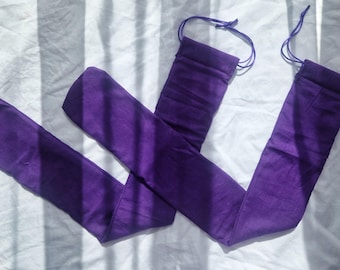 Puede incluir: Un par de calentadores de piernas largos de color púrpura intenso con cierres de cordón en la parte superior. Los calentadores de piernas están hechos de una tela suave y están colocados sobre una superficie blanca, con sombras proyectadas sobre ellos.