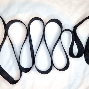 May include: Black webbing strap with white stitching. The strap is folded into a series of loops.