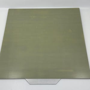 Könnte beinhalten: Ein rechteckiges, strukturiertes, hitzebeständiges Druckbett in Grün mit einer silbernen Metallverkleidung.