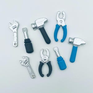 May include: A collection of miniature tools, including wrenches, screwdrivers, hammers, and pliers. The tools are silver with black and blue handles, arranged on a white surface. The tools are likely for a craft or model-making project.