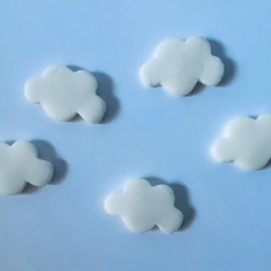 May include: Five white cloud-shaped decorations are scattered on a light blue background. The clouds have a soft, rounded shape, and are evenly spaced. The image has a clean, minimalist aesthetic.