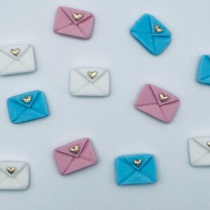 May include: Assortment of small, decorative envelopes with a heart design. The envelopes are in pink, blue, and white with gold hearts.