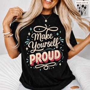 Peut inclure: Un t-shirt noir à manches courtes avec le texte "Make Yourself PROUD" écrit dans une police stylisée. Le motif comprend des volutes décoratives, des petites étoiles et des points de couleur crème, bleu clair et rouge au centre du vêtement.