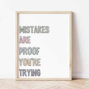 May include: A framed print with the text "Mistakes are proof you're trying" in a colourful, layered font style. The print is in a light wood frame and is on a light wood floor.