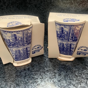 May include: Two Ringtons Millennium 2000 fine bone china beakers in their original cardboard packaging. Each white beaker features blue illustrations of cathedral architecture, a gold rim, and the Ringtons Millennium 2000 logo printed on the front.