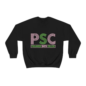 Pode incluir: Camisola preta com as letras "PSC" em rosa e verde, com as palavras "Philander Smith College" por baixo. As letras são feitas de pequenos pontos. Uma parte de cima casual e confortável.