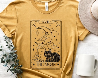 May include: A mustard yellow t-shirt with a black and white tarot card design featuring the moon and a black cat. The card reads "XVIII THE MOON".