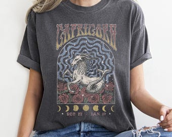 Könnte beinhalten: Dunkelgraues T-Shirt mit einem Sternzeichen-Design für Steinbock. Die Grafik zeigt ein Ziegen-Fisch-Hybrid, Rosen und den Text "CAPRICORN" in einem Vintage-Schriftstil. Das Shirt zeigt auch die Daten "DEC 22 - JAN 19" und Mondphasen.