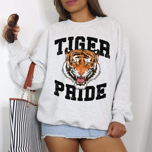 Op de afbeelding: Een grijs sweatshirt met een zwart en oranje tijgerprint en de tekst "Tiger Pride" gedrukt op de voorkant.