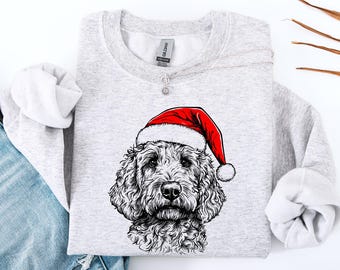 May include: A light grey sweatshirt with a detailed black and white illustration of a dog wearing a red Santa hat. The sweatshirt has a crew neck and long sleeves, ideal for the festive season.