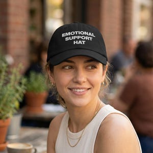 May include: A white ceramic mug with a black handle and the text "But First, Coffee" in a bold, black font. The mug is set against a blurred background, suggesting a cozy setting.