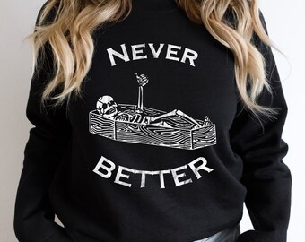May include: Black sweatshirt with the words "NEVER BETTER" in white, above a white illustration of a skeleton in a coffin. The skeleton is giving a thumbs up. The sweatshirt is a crew neck.