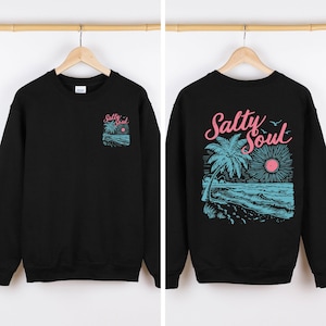 Può includere: Felpa nera con un disegno a tema spiaggia. La parte anteriore presenta un piccolo design a tasca con una palma, l'oceano e le parole "Salty Soul". Il retro mostra un design più grande con una palma, il sole, le onde e le parole "Salty Soul."
