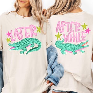 May include: Cream-colored t-shirts with a playful design. The front of the shirt features the word "LATER" in pink, with a green alligator illustration. The back of the shirt has the words "AFTER WHILE" and a matching alligator.