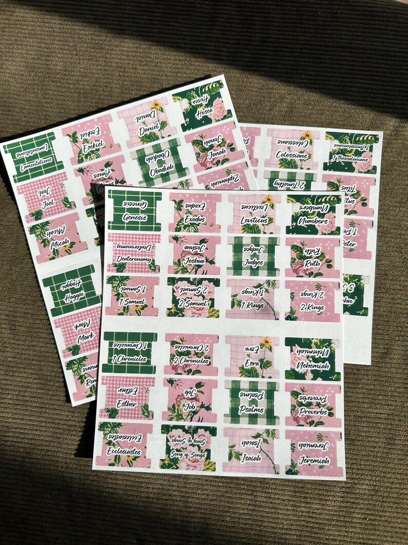 May include: Sheets of Bible book tabs with floral and gingham patterns. The tabs are labeled with book names like Genesis, Exodus, and Proverbs. The tabs are in pink, green, and white.
