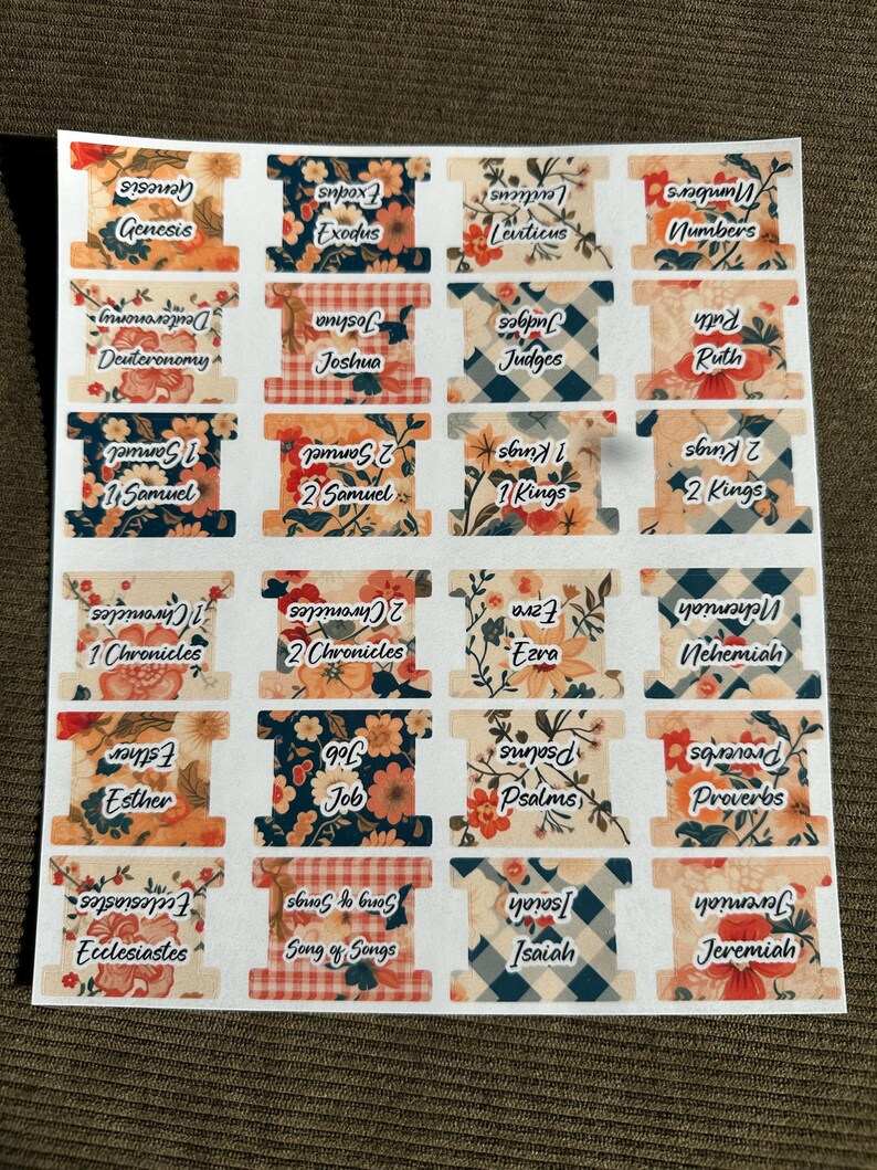 May include: A sheet of Bible book tabs with floral, plaid, and patterned designs. Each tab features the name of a book of the Bible in white text. The tabs are in various colors, including orange, blue, and red.