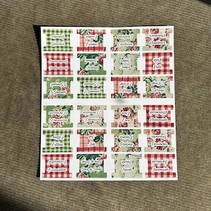 May include: Sheet of Bible verse labels with various patterns, including red and green gingham, floral, and solid colors. Each label features a book of the Bible, such as Genesis, Exodus, and Psalms, in a white font.