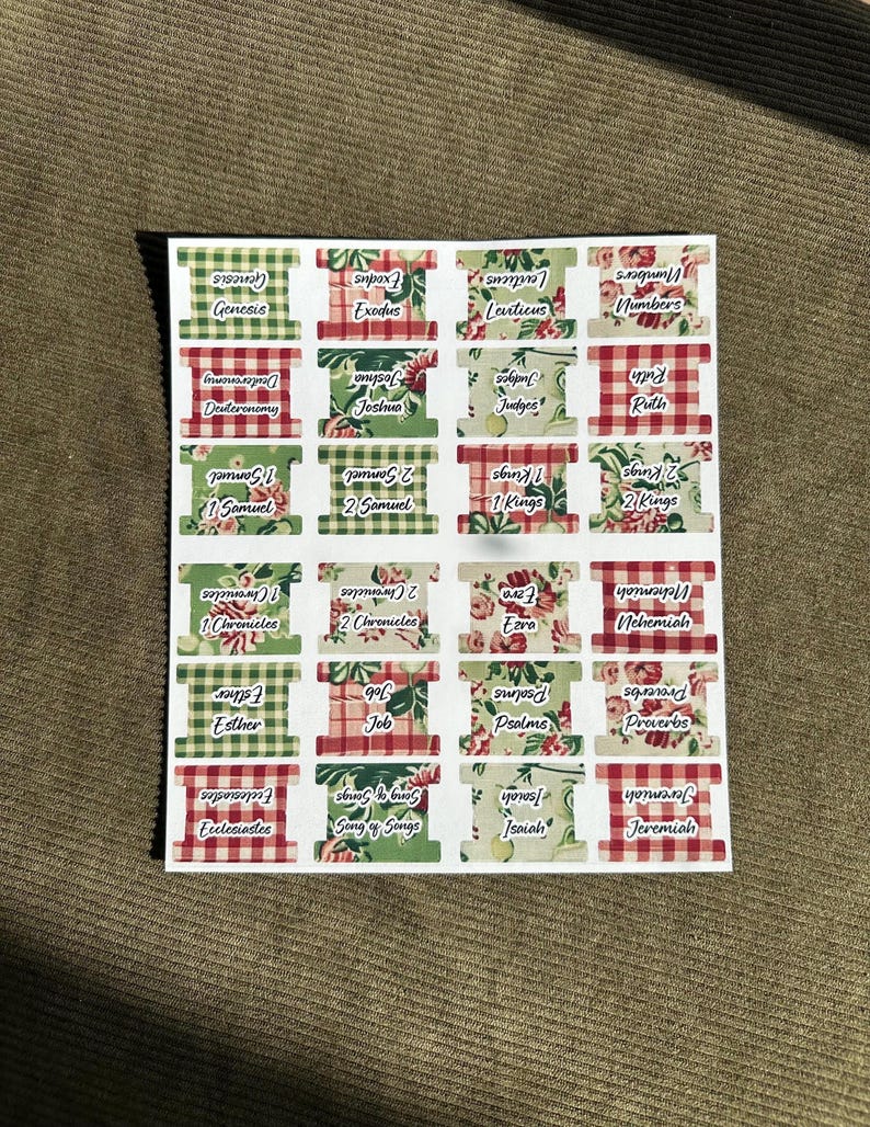 May include: Sheet of Bible verse labels with various patterns, including red and green gingham, floral, and solid colors. Each label features a book of the Bible, such as Genesis, Exodus, and Psalms, in a white font.