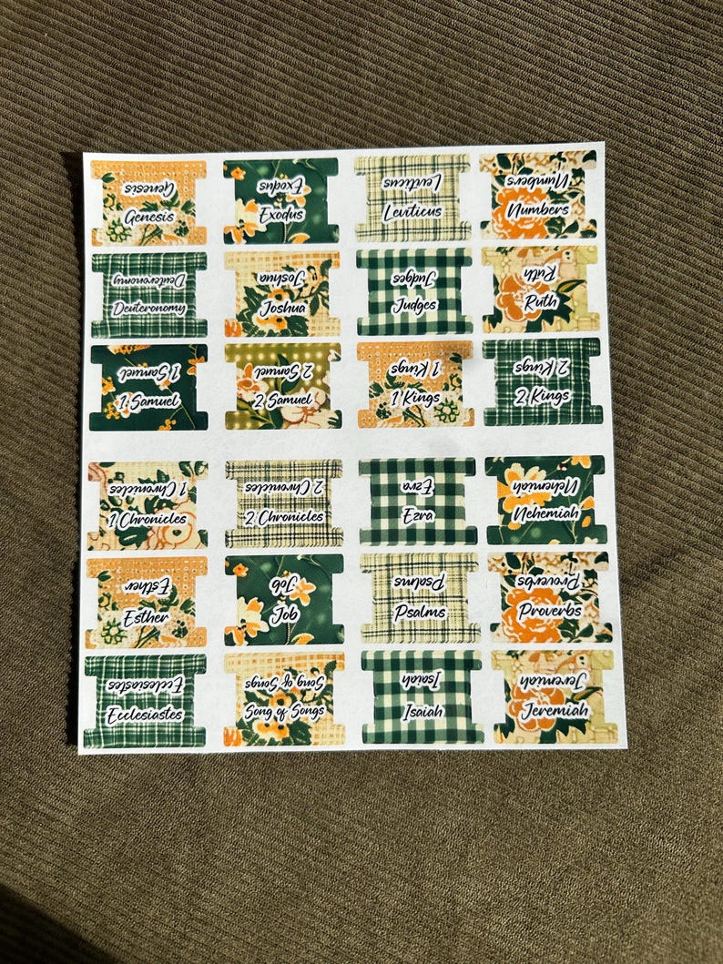 May include: A sheet of Bible book labels with various floral and plaid patterns. Each label features the name of a book from the Bible, such as Genesis, Exodus, and Proverbs. The labels are rectangular with a decorative spool-like design.