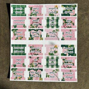 May include: A sheet of decorative Bible book labels. The labels feature a mix of floral and checkered patterns in pink and green. Each label displays a book of the Bible in a handwritten font.