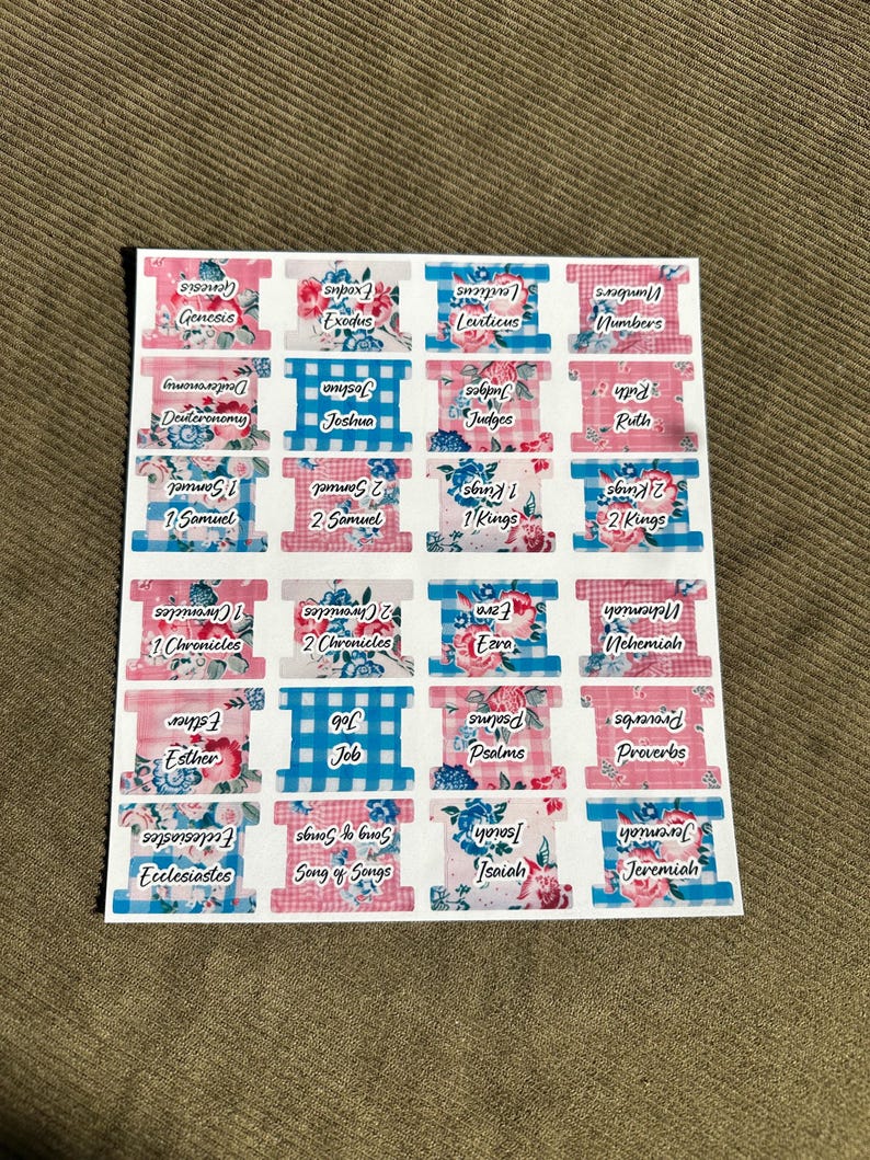 May include: A sheet of Bible book tabs with floral and gingham patterns. Each tab is labeled with a book of the Bible, such as Genesis, Exodus, and Proverbs. The tabs are in shades of pink, blue, and white.