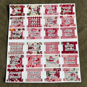 May include: A sheet of Bible book tabs with floral and gingham patterns in shades of pink and red. Each tab features the name of a book of the Bible in white text, such as Genesis, Exodus, and Proverbs.