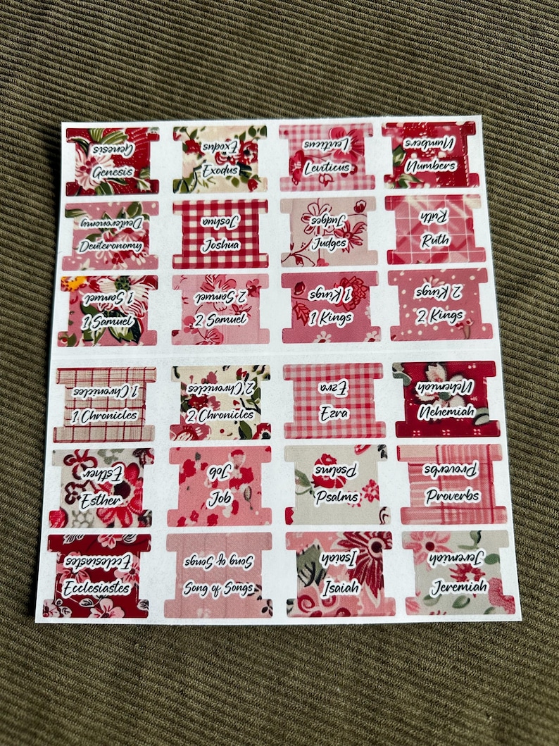 May include: A sheet of Bible book tabs with floral and gingham patterns in shades of pink and red. Each tab features the name of a book of the Bible in white text, such as Genesis, Exodus, and Proverbs.
