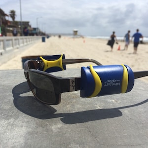 May include: A pair of sunglasses with blue and yellow floaters attached to the arms. The floaters have the text "EyeFloats" printed on them.