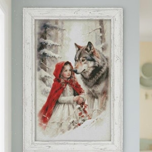 May include: Framed artwork showing a girl in a red cloak and a wolf in a snowy forest. The girl holds a basket of red flowers. The artwork is in a white distressed frame, giving a vintage feel.