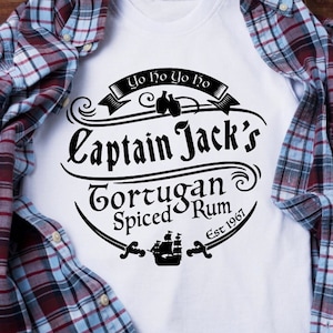 May include: White t-shirt with a black and white graphic design of a logo for Captain Jack's Tortugan Spiced Rum. The logo features a ship, two bottles, and the text "Yo ho yo ho" and "Est 1967".