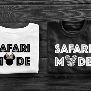 K&ouml;nnte beinhalten: Zwei wei&szlig;e T-Shirts mit schwarzem Text, der "Safari Mode" lautet, und einem schwarzen und wei&szlig;en Mickey-Maus-Kopf mit Schleife. Ein Shirt ist wei&szlig; und das andere ist schwarz.