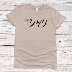 May include: A beige t-shirt with the Japanese text "Tシャツ" printed in black on the front.