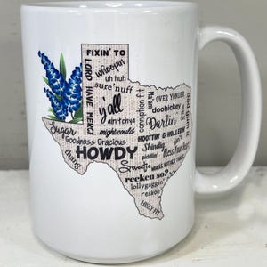 May include: White ceramic mug featuring a Texas-shaped design with the word "Howdy" and other Texan slang terms. The mug also includes a bluebonnet flower illustration, a state flower of Texas.