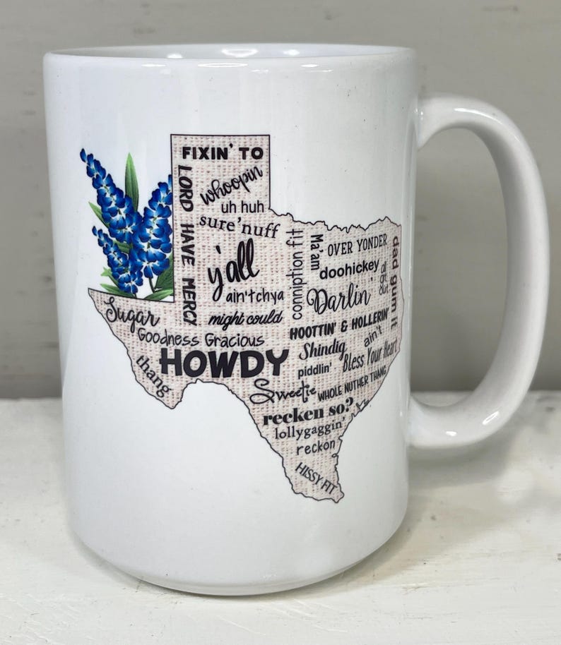 May include: White ceramic mug featuring a Texas-shaped design with the word "Howdy" and other Texan slang terms. The mug also includes a bluebonnet flower illustration, a state flower of Texas.