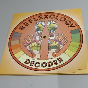 May include: A reflexology decoder with a circular design featuring illustrations of feet and hands, with the text "REFLEXOLOGY DECODER" in a circular pattern. The color palette includes shades of orange, brown, and yellow.