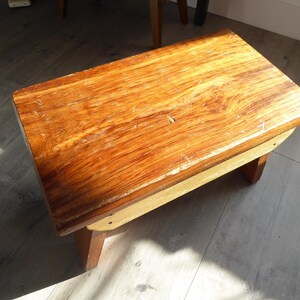 May include: A small, rectangular wooden step stool with a warm, reddish-brown finish. The stool has a simple design with four short legs and a flat top, measuring approximately 46 cm long and 25 cm wide.