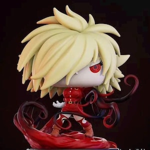 Puede incluir: Figura estilizada con un gran peinado puntiagudo de color amarillo claro y ojos rojos. La figura viste un atuendo rojo y se apoya sobre una base roja con detalles en rojo oscuro. El diseño general tiene una estética de dibujos animados.