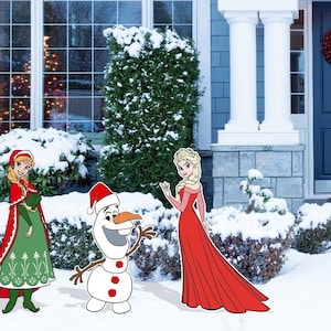 May include: A snowman wearing a Santa hat stands next to two girls in winter outfits. The girl on the left is wearing a red and green dress with a red cape. The girl on the right is wearing a red dress. The scene is set in front of a house with a blue door and a snowy yard.