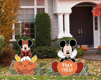 Puede incluir: Decoraciones de jardín de Halloween de Mickey Mouse y Minnie Mouse. Mickey está sentado en una calabaza que dice "Trick or Treat". Minnie está sentada en una calabaza tallada con forma de calavera.