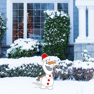 May include: A snowman wearing a red Santa hat and a carrot nose stands in a snowy yard in front of a house with a Christmas tree in the window.