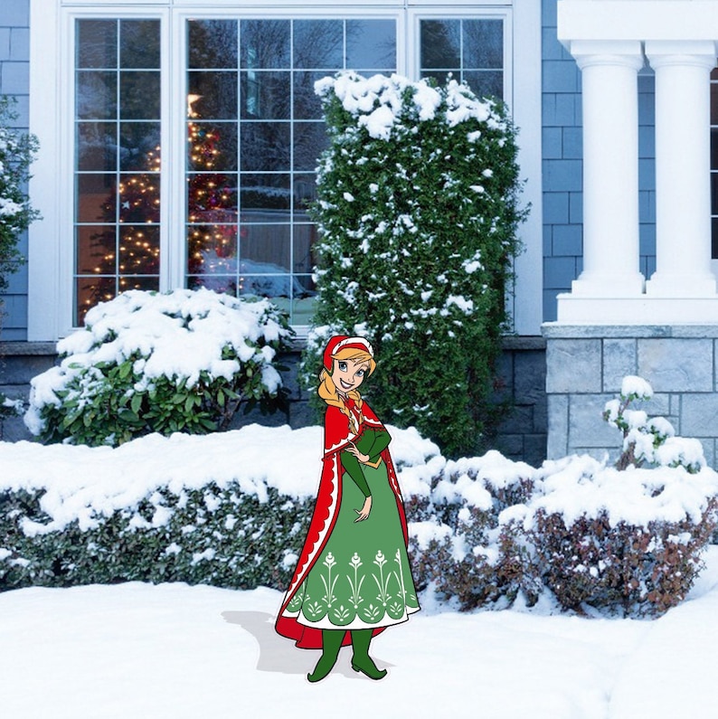 May include: A cartoon illustration of a young woman wearing a red hooded cloak and a green dress with white snowflake designs. She is standing in a snowy yard with a Christmas tree visible in the window behind her.