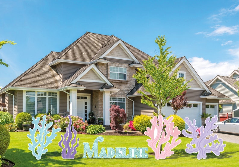 May include: Lawn decorations spelling out "Madeline" with coral and seaweed designs in shades of blue, purple, and pink. The decorations are placed on a green lawn in front of a house.