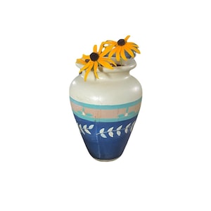Könnte beinhalten: Eine Keramikvase mit einem cremefarbenen oberen Teil, einem hellrosa Band und einem dunkelblauen unteren Teil mit einem weißen Blattmuster. Zwei gelbe Blumen mit dunkelbraunen Mitten stecken in der Öffnung der Vase.