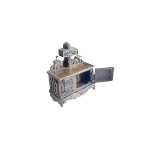 Op de afbeelding: Een vintage metalen potloodpuntenslijper in de vorm van een gietijzeren fornuis met een open deur. Het fornuis is geschilderd in tinten bruin en goud met ingewikkelde details.